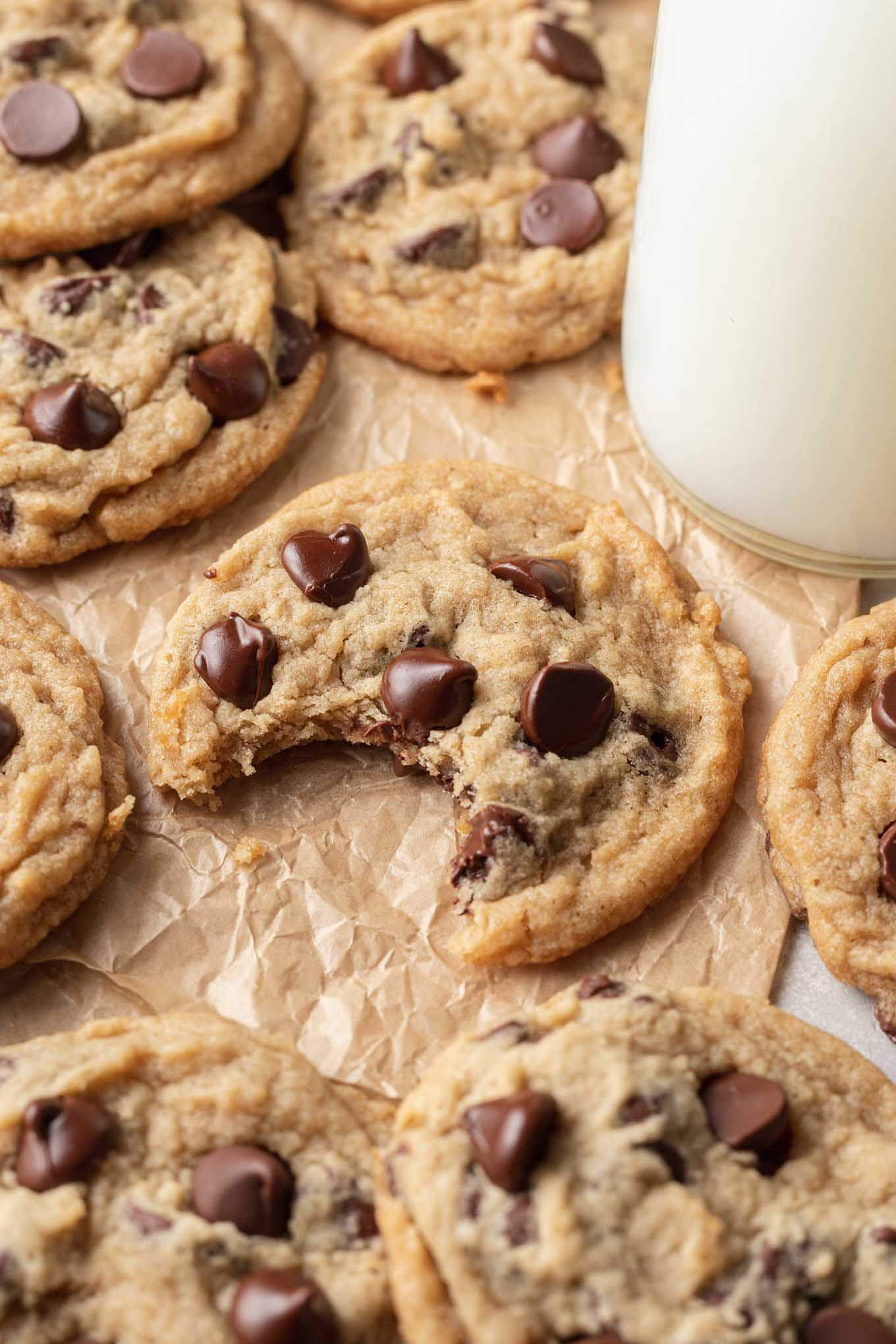 Eggless chocolate chip cookies surrounding a glass of milk. The center cookie has a bite missing. 