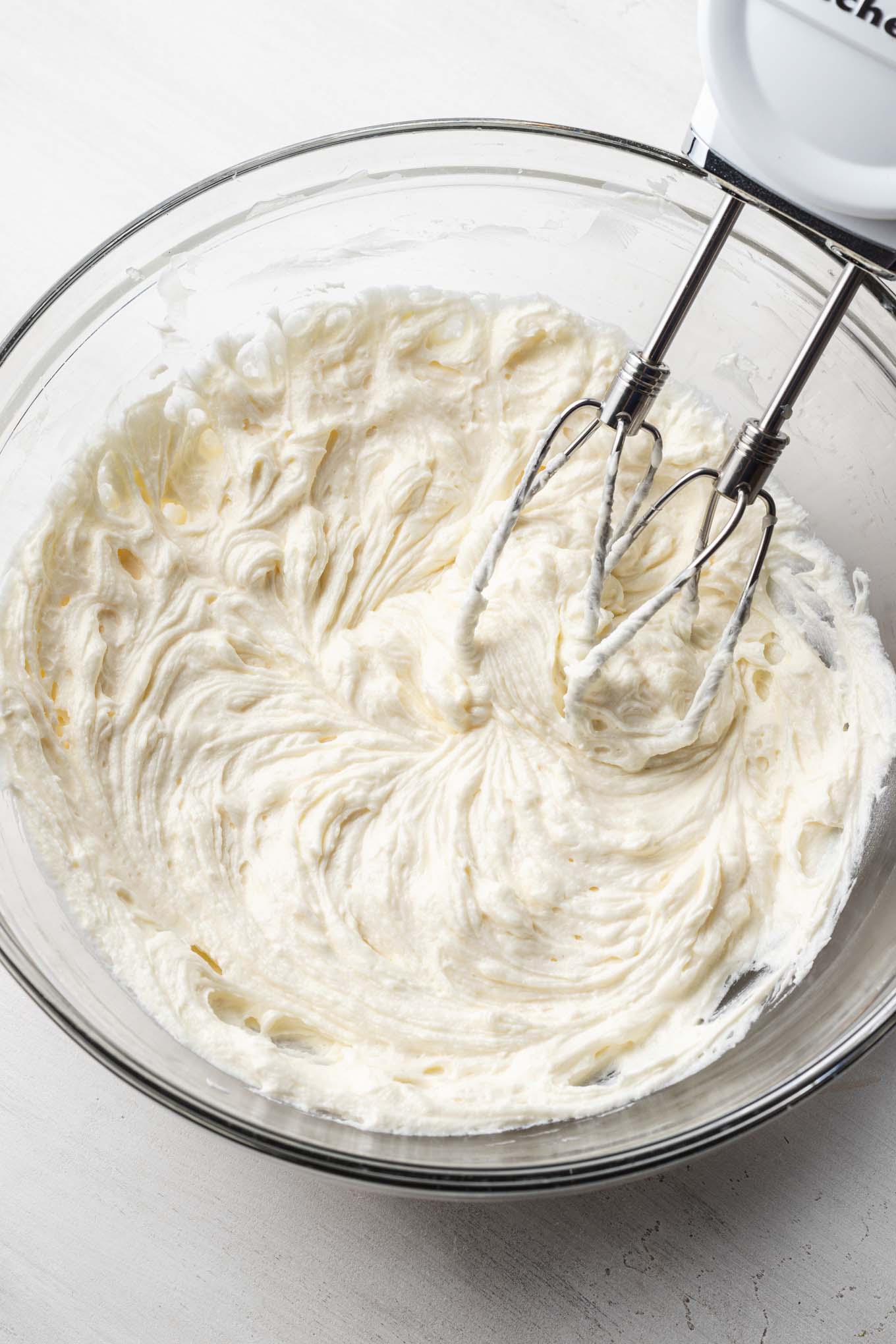 A glass mixing bowl with creamed butter. A handheld mixer rests on the side.