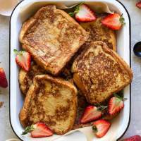 A baking pan filled with finished French toast surrounded by strawberries and spices.