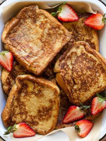 A baking pan filled with finished French toast surrounded by strawberries and spices.