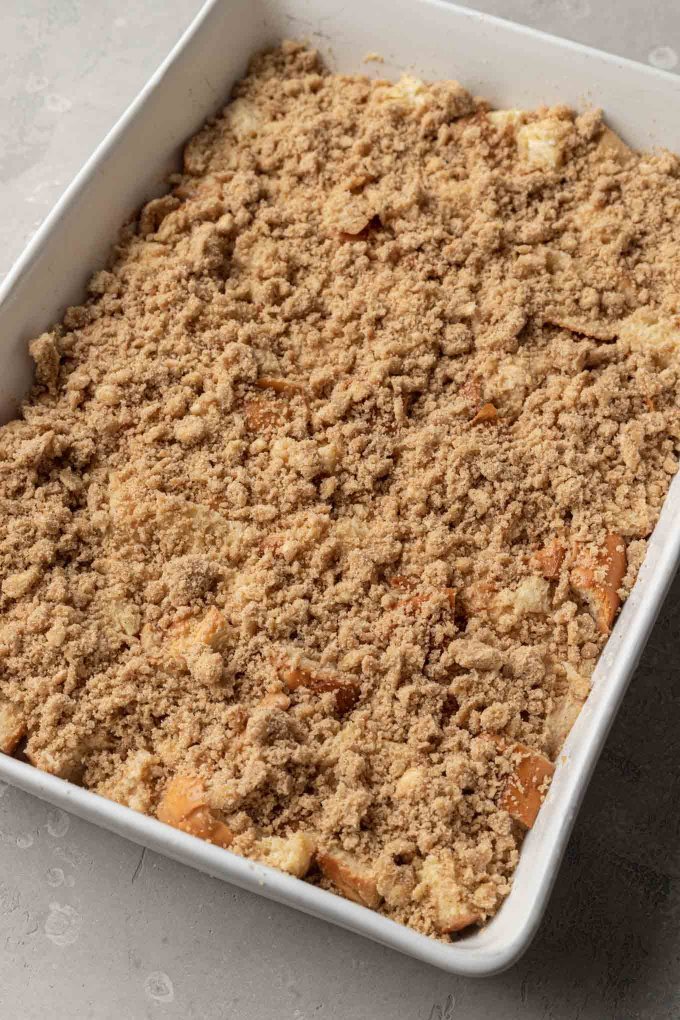 Unbaked challah french toast casserole in a white baking dish with the crumb topping added. 