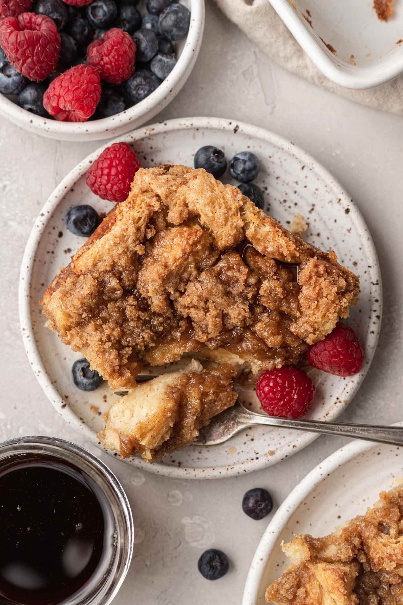 An overhead view of a serving of baked french toast casserole, with fresh berries on the side. 