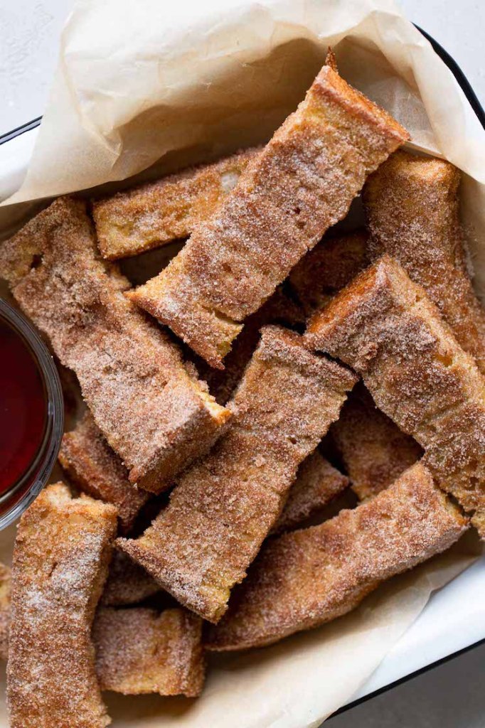 Overhead view of baked french toast sticks piled in a baking dish. A small bowl of maple syrup is also in the dish. 