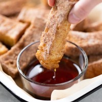 A baked french toast stick being dunked into a small dish of maple syrup.