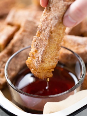 A baked french toast stick being dunked into a small dish of maple syrup.