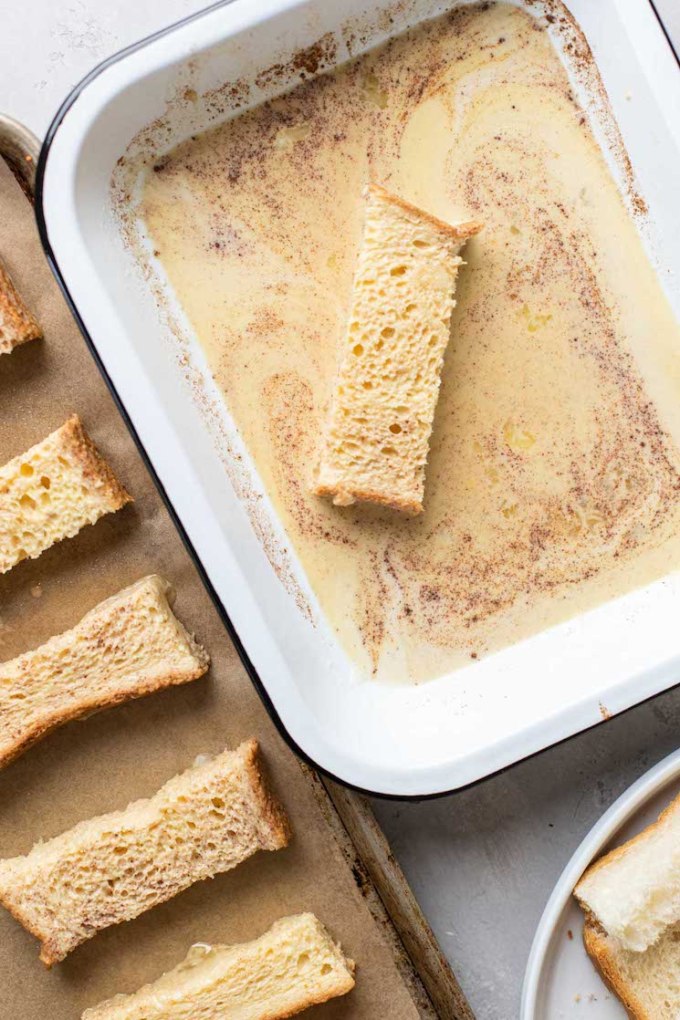 Process shot of Texas Toast slices being dunked one by one into a baking dish filled with french toast batter.