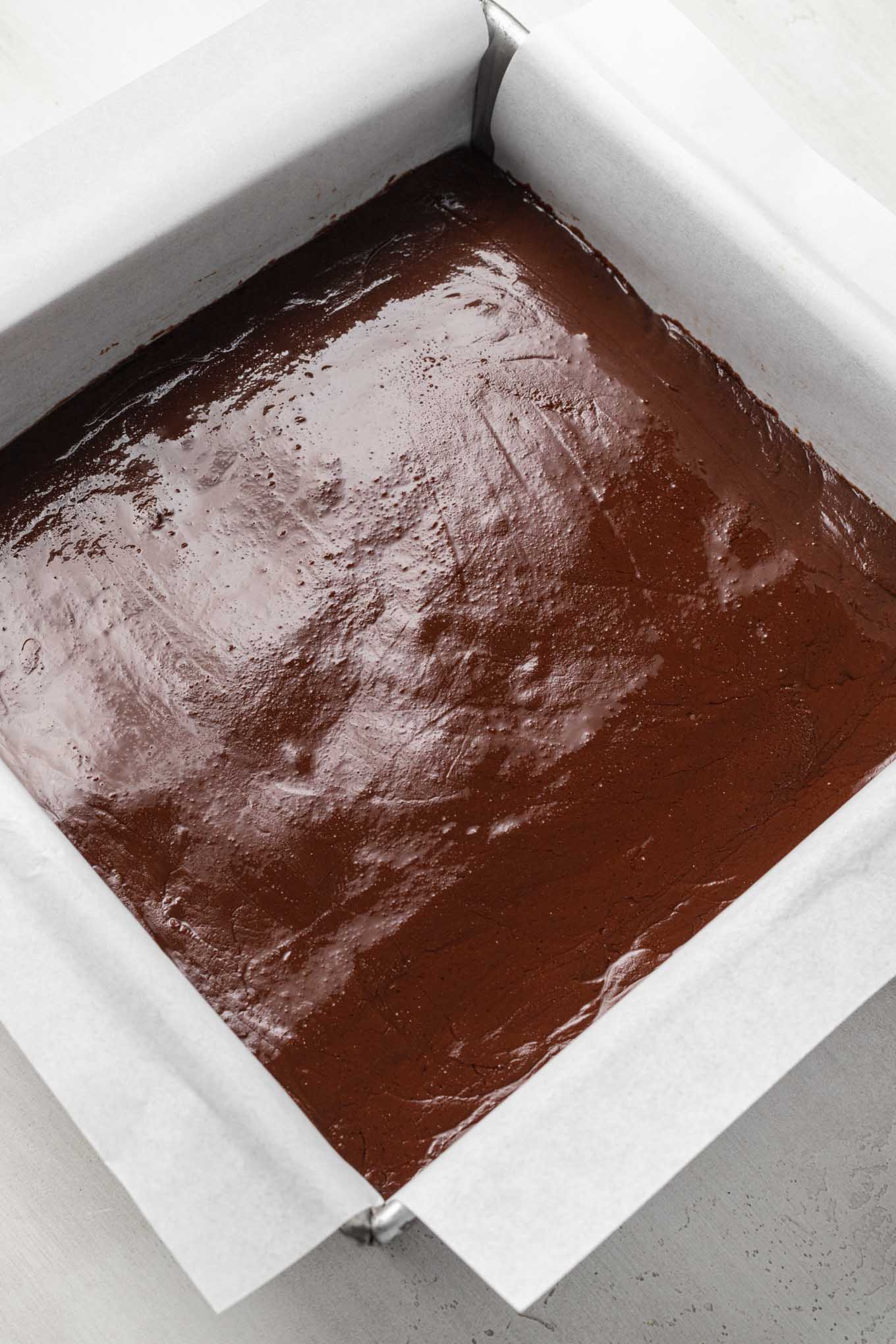 Melted chocolate fudge in a baking pan lined with parchment paper. 