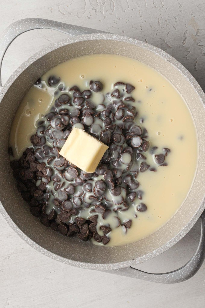 An overhead view of sweetened condensed milk, chocolate chips, and butter in a saucepan.
