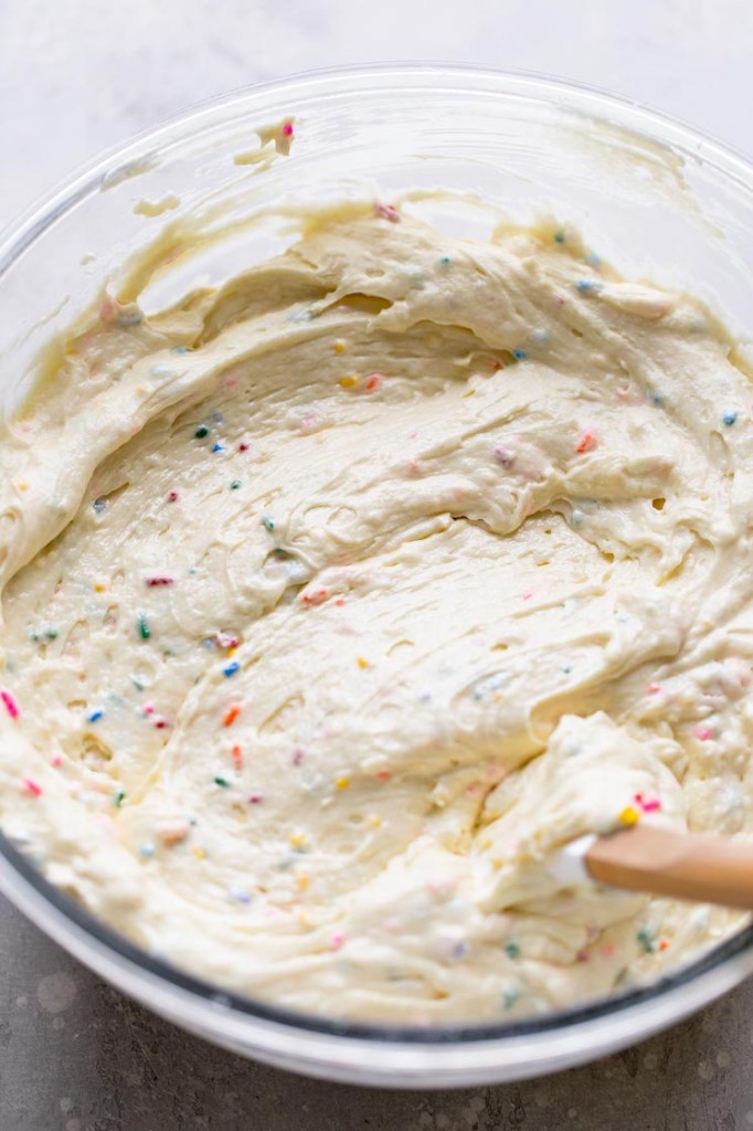 An overhead view of funfetti cake batter in a glass mixing bowl with a rubber spatula. 