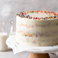 A homemade funfetti cake on a cake stand. Two glass bottles of milk are in the background.