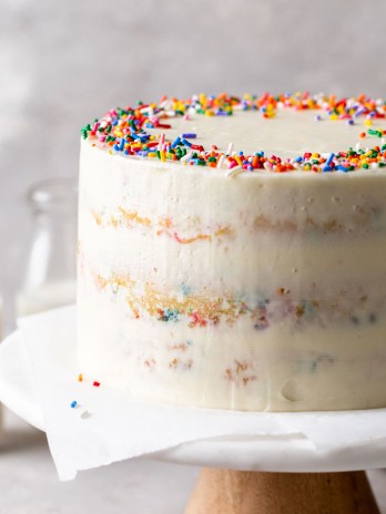 A homemade funfetti cake on a cake stand. Two glass bottles of milk are in the background.