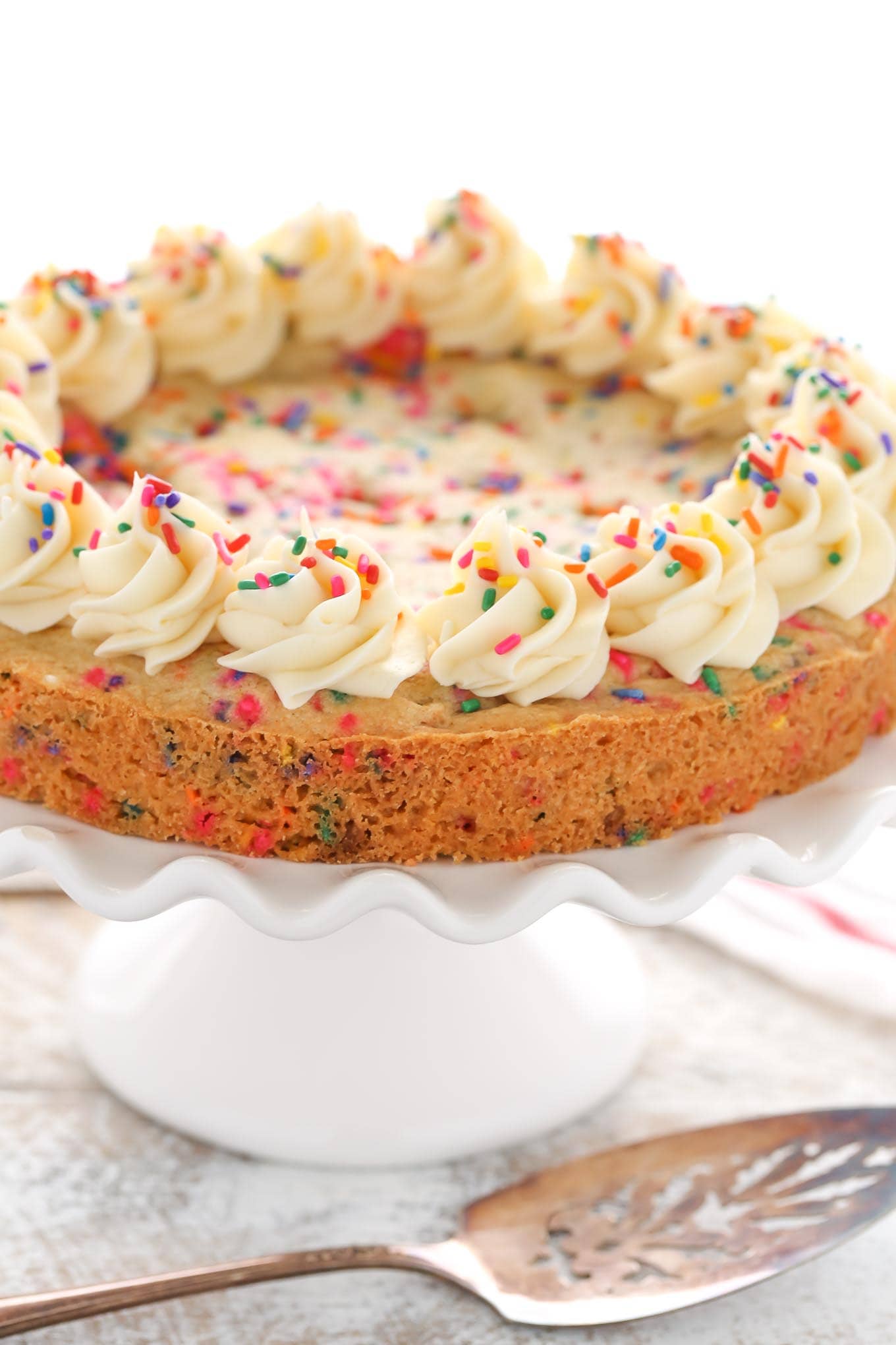 A sugar cookie cake topped with whirls of vanilla buttercream, seen from the side. 