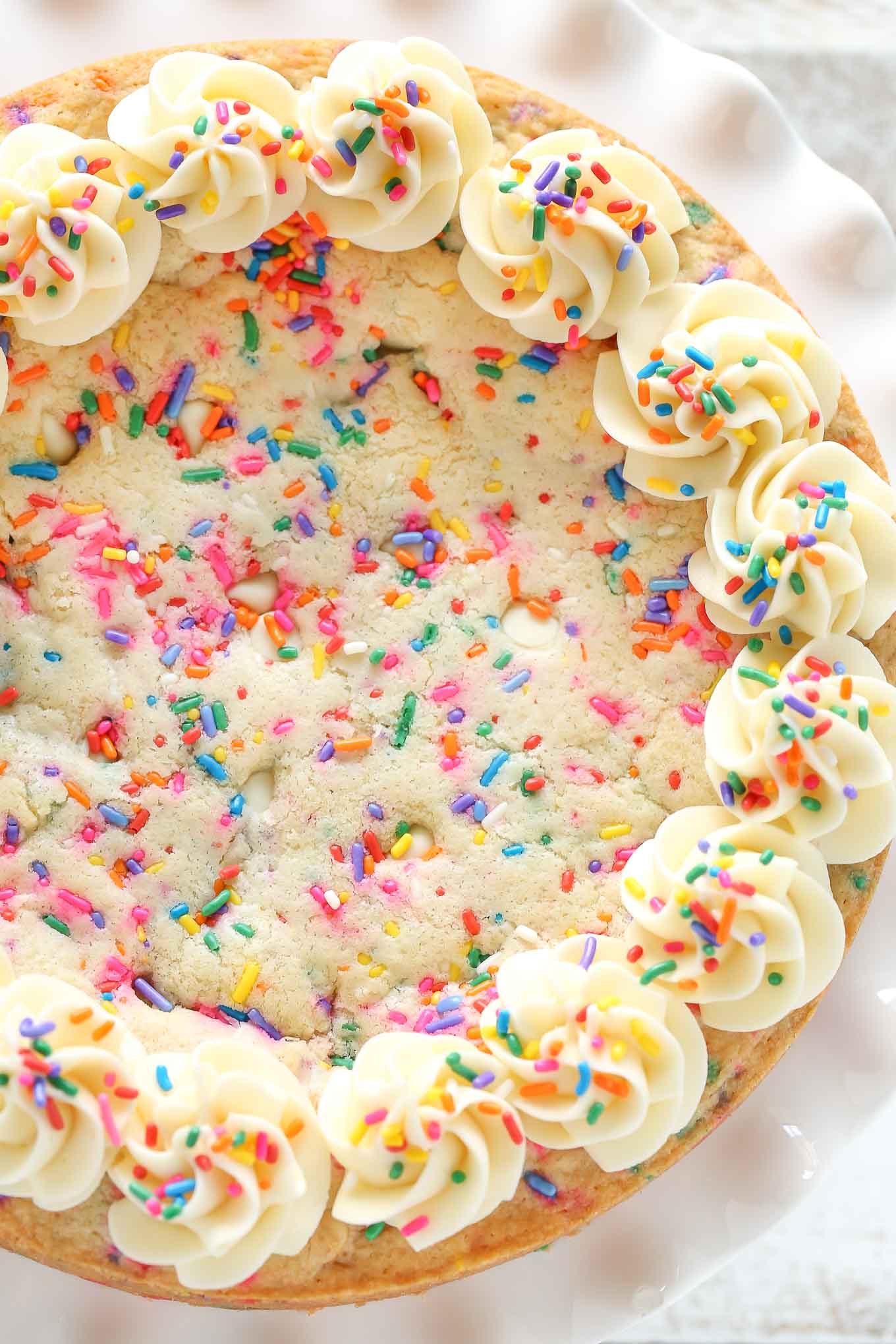 Overhead view of a birthday cookie cake topped with sprinkles and vanilla frosting. 