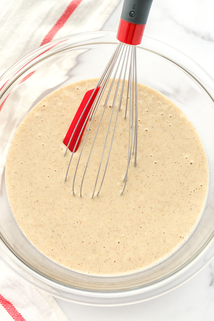 A clear glass bowl filled with funnel cake batter and a whisk. 