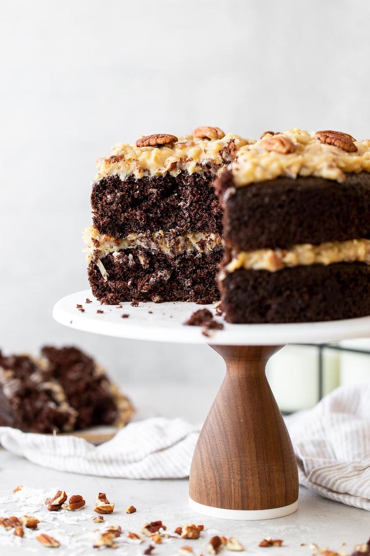 A layered German Chocolate Cake on a marble cake stand with a slice taken out to show the layers more clearly.