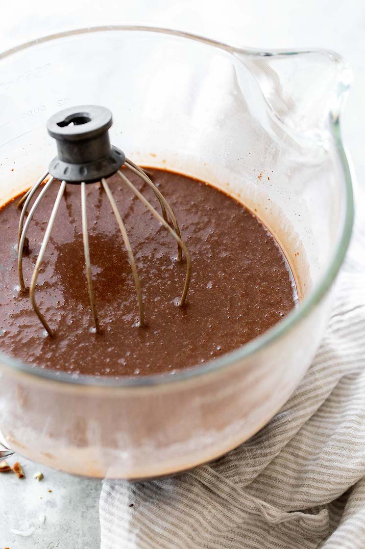 A glass mixing bowl filled with chocolate cake batter with the whisk still in the bowl.