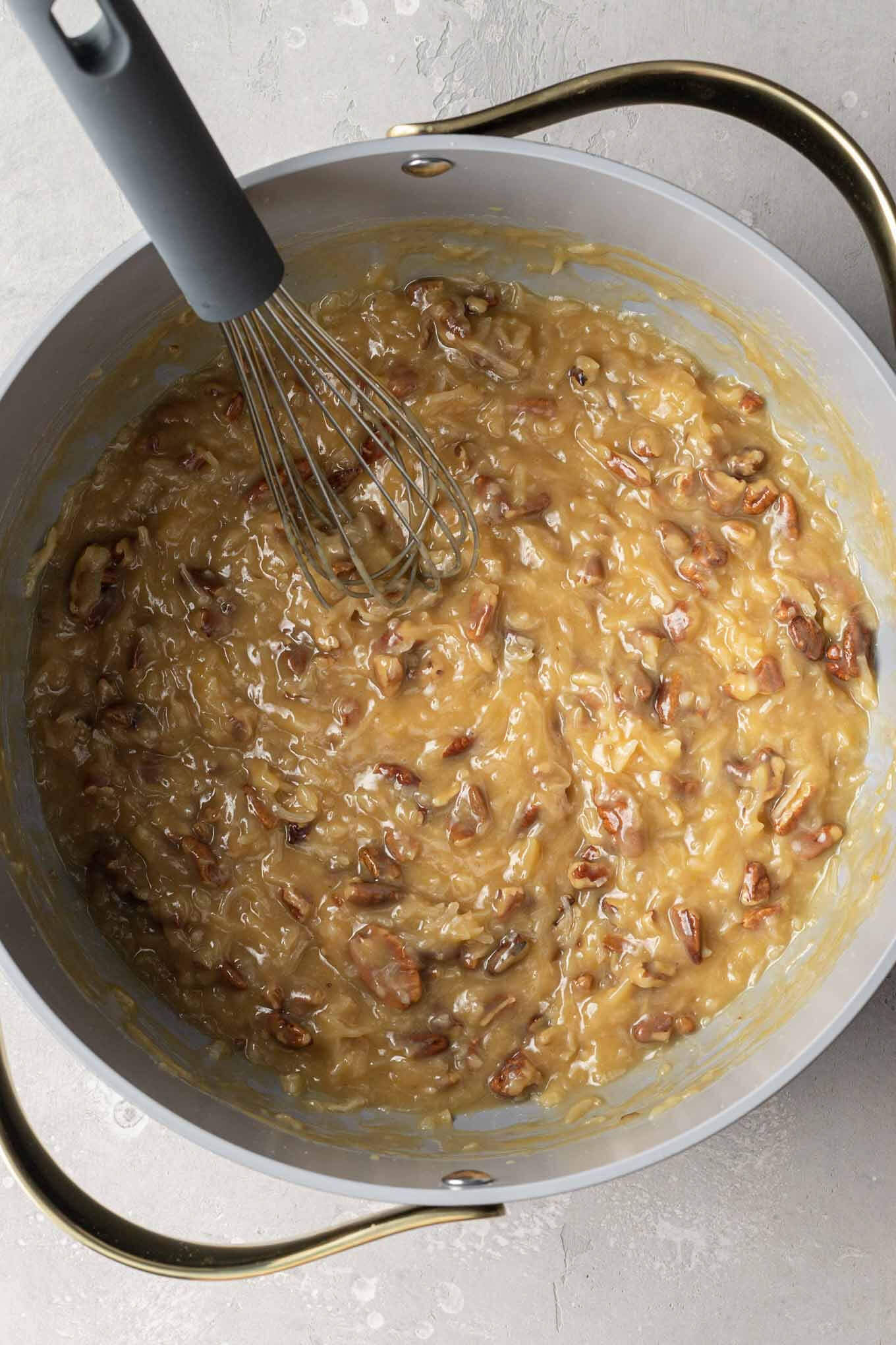 An overhead view of German chocolate cake frosting in a saucepan with a whisk. 