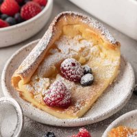 A slice of German pancake dusted with powdered sugar and topped with fresh berries.