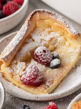 A slice of German pancake dusted with powdered sugar and topped with fresh berries.