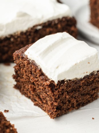 A slice of gingerbread cake topped with homemade whipped cream. The rest of the cake is in the background.