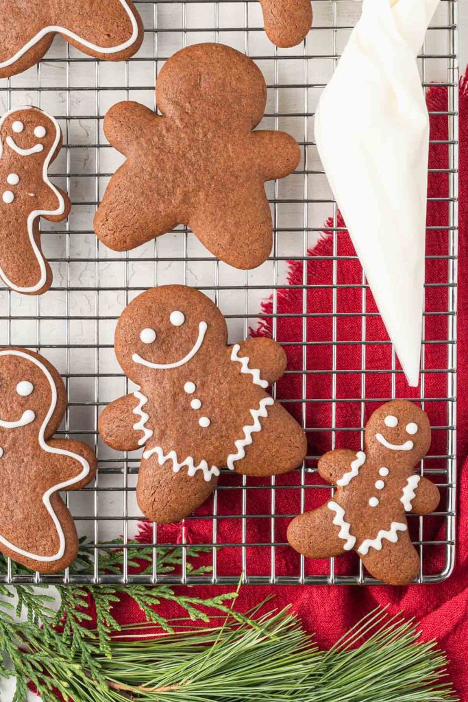 An overhead view of soft gingerbread cookies with icing and a piping bag on a wire rack. 