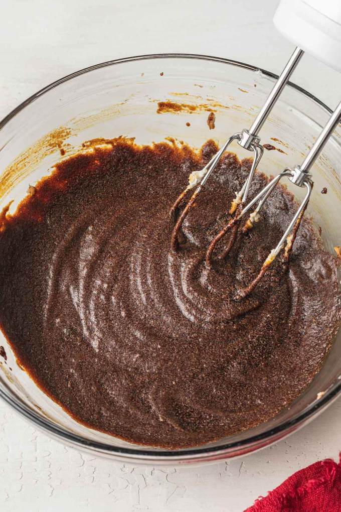 An overhead view of a glass mixing bowl filled with the wet ingredients for gingerbread dough.