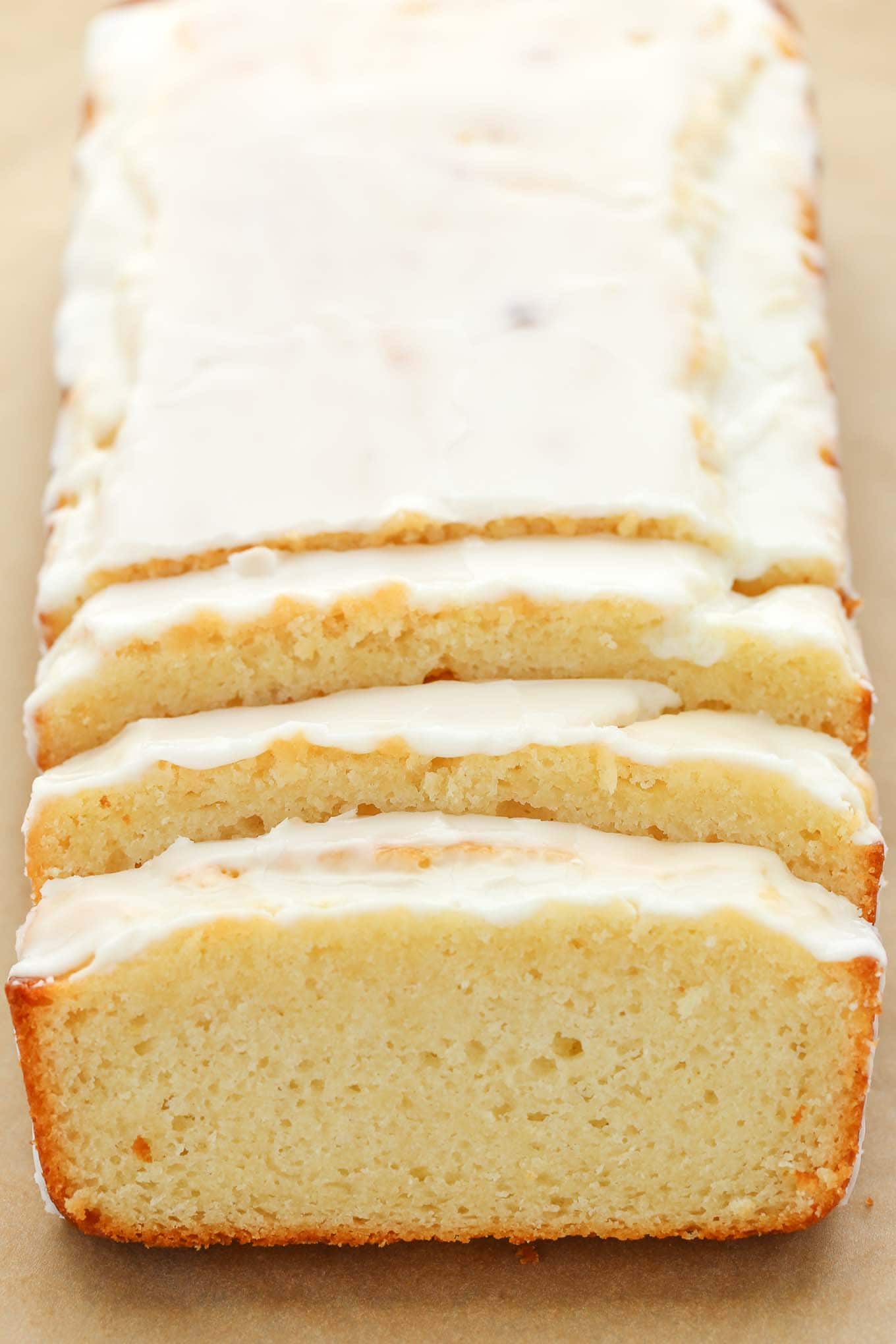 A loaf of lemon bread with glaze on top. Three slices have been cut from the front. 