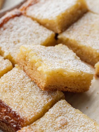 Several sliced gooey butter bars on a piece of brown parchment paper.