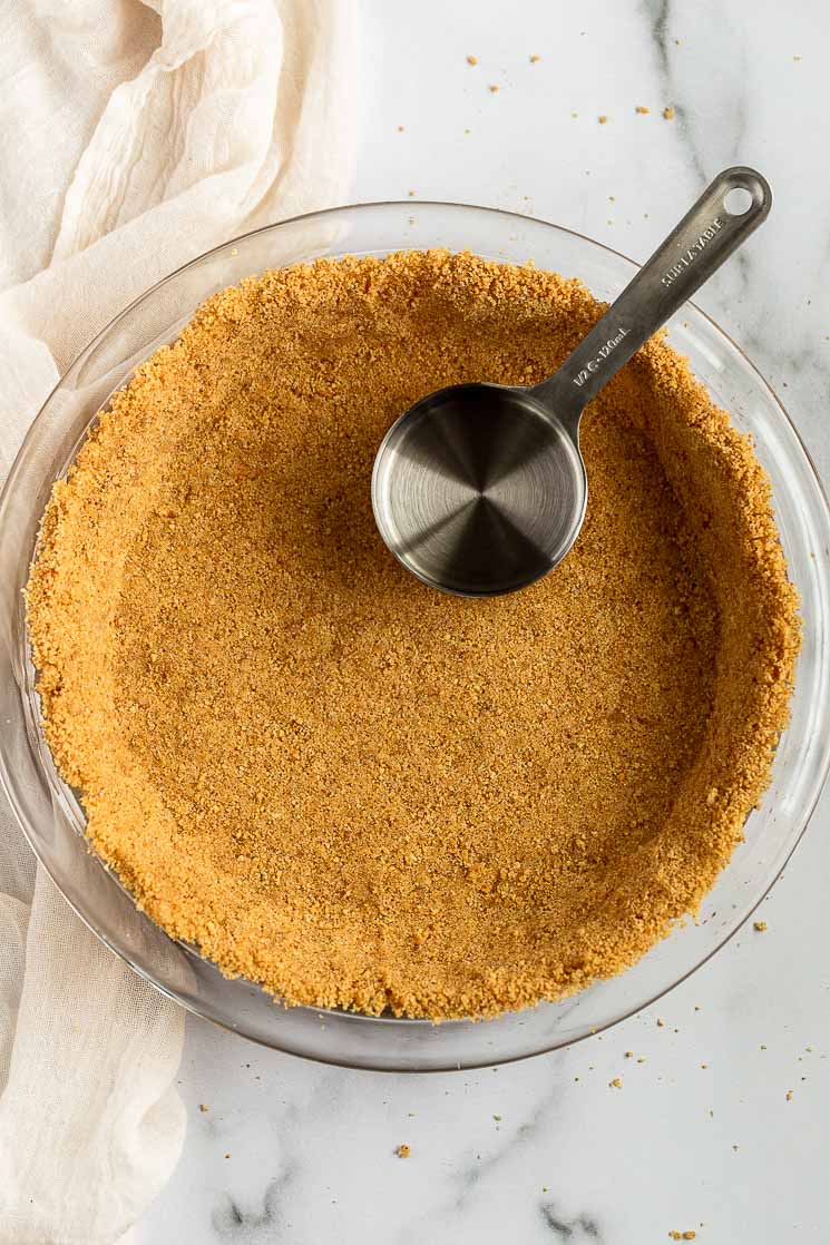 A graham cracker crusted pressed into a pie plate with a measuring cup on the side.