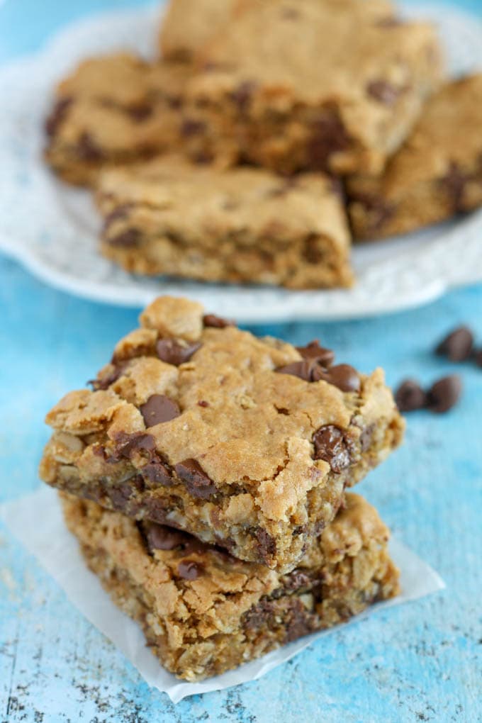 A stack of two oatmeal bars on a square of parchment paper. Additional bars rest on a plate in the background. 