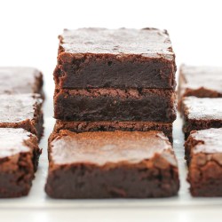 A stack of sliced brownies on parchment paper with more brownies around it.