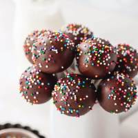 Several chocolate cake pops topped with sprinkles in a small white jar.