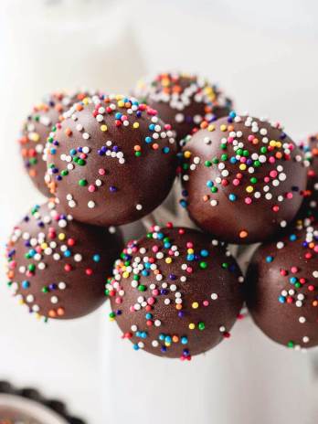 Several chocolate cake pops topped with sprinkles in a small white jar.