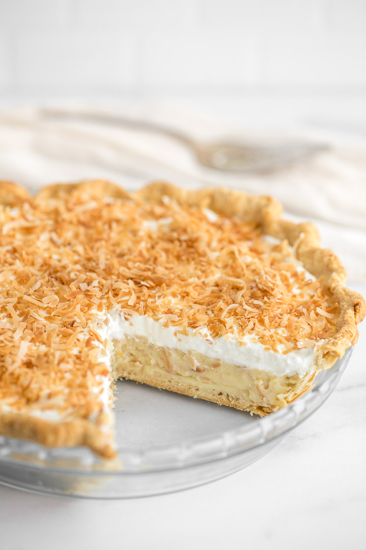 A close-up of a coconut cream pie with a slice taken out of it.