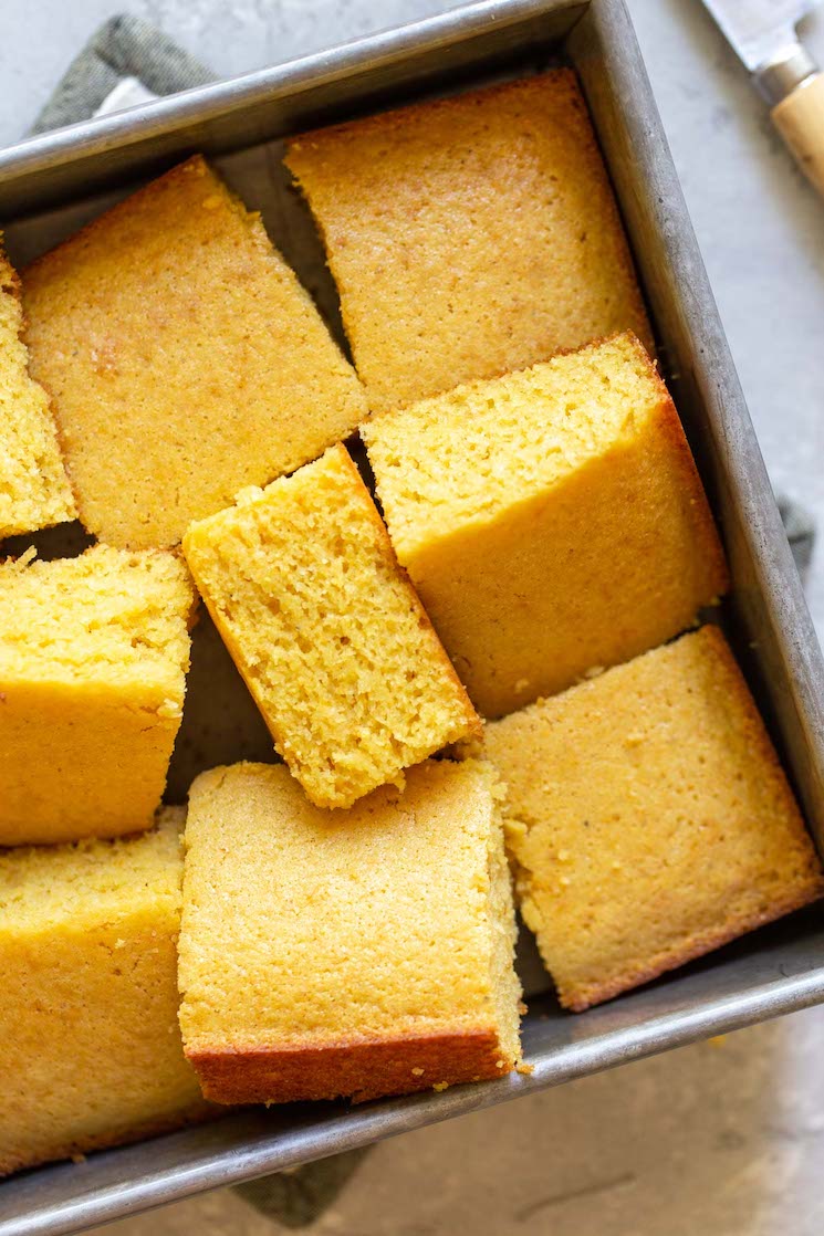 A pan of cornbread pieces cut and laid randomly into a metal baking pan showing different perspectives of each piece.