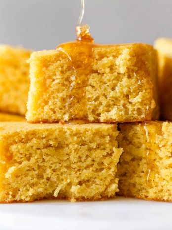 A stack of square cornbread slices with honey being drizzled on top.