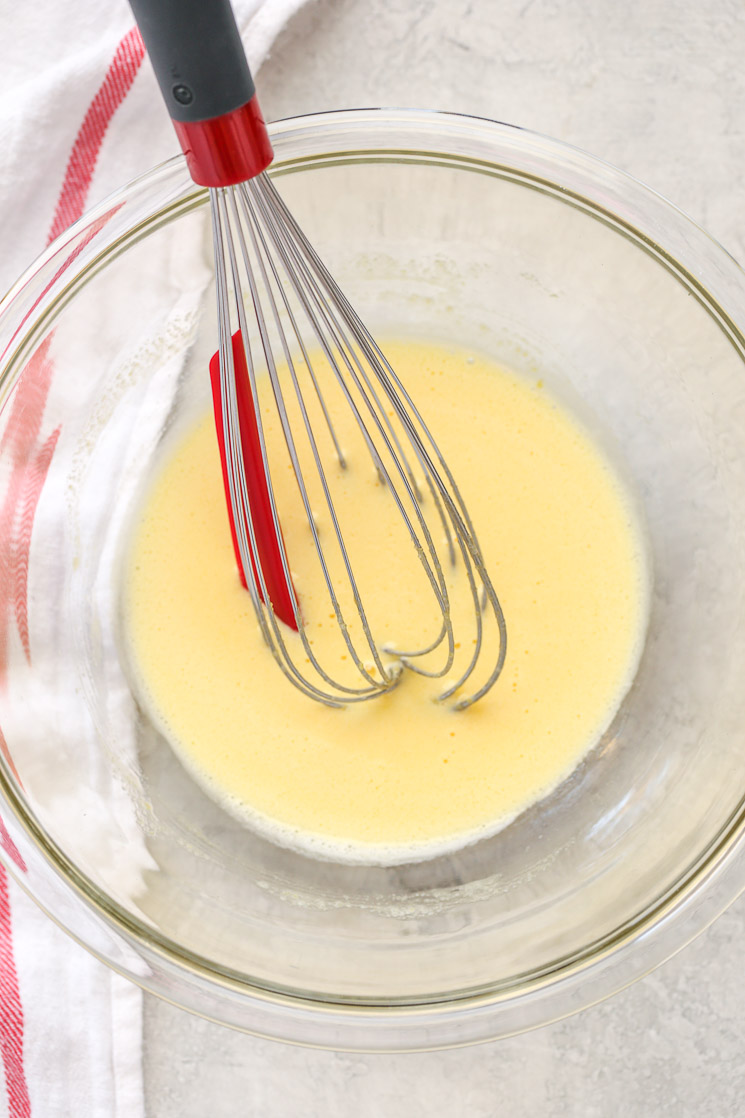 A clear glass bowl filled with egg yolks whisked with sugar and a white napkin on the side.