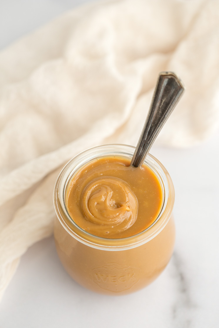 A glass jar filled with dulce de leche and an antique spoon for serving. 