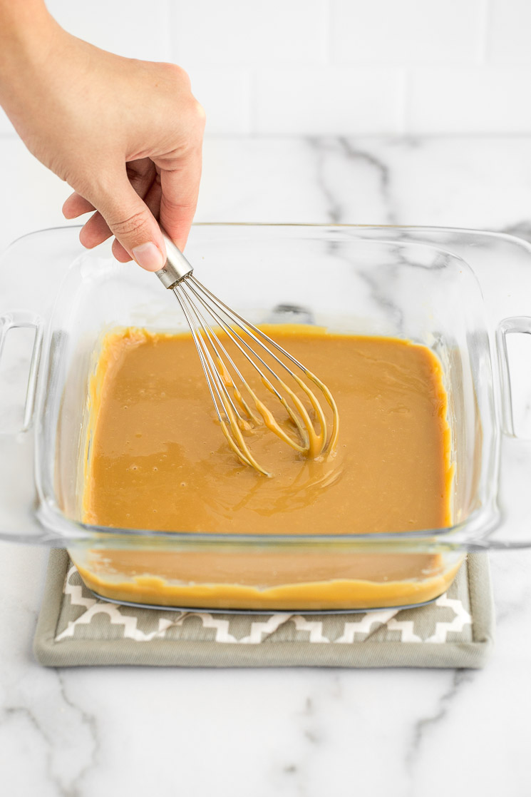 A clear baking dish with finished dulce de leche being wisked to get it to the proper consistency.