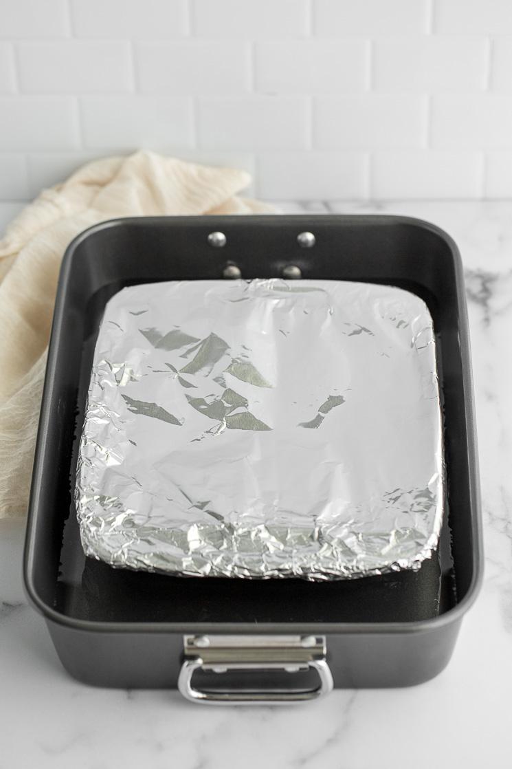 A baking dish with sweetened condensed milk covered in foil inside of a roasting pan.
