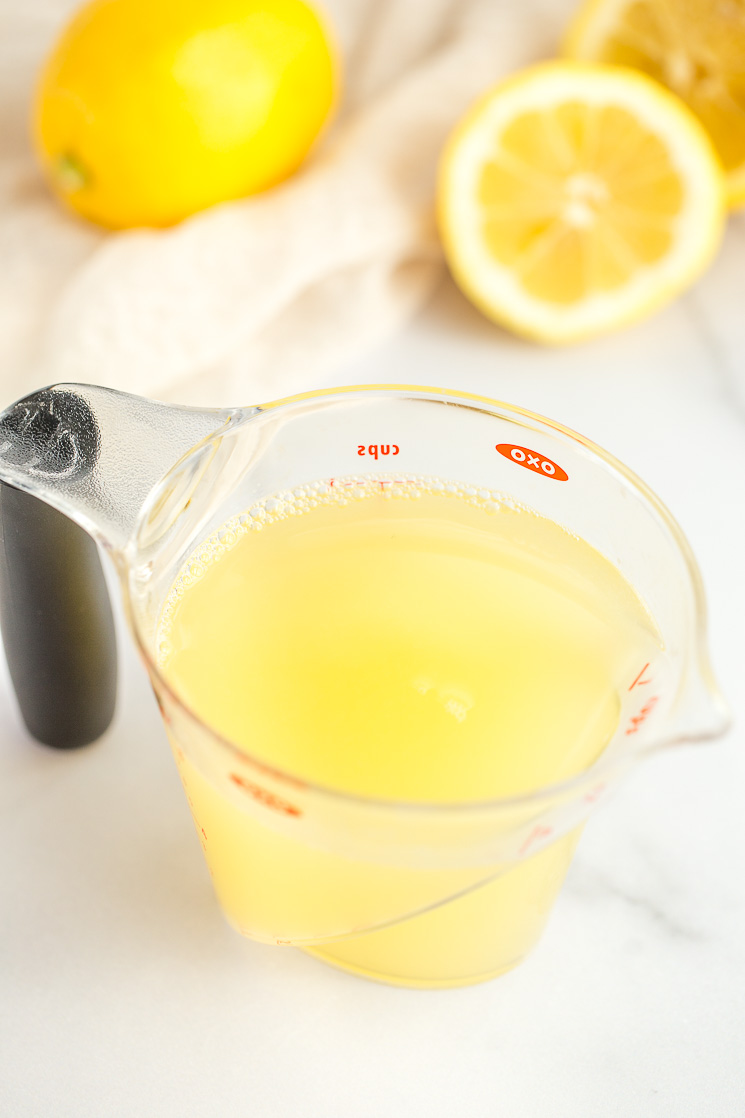 A clear measuring cup filled with fresh lemon juice.