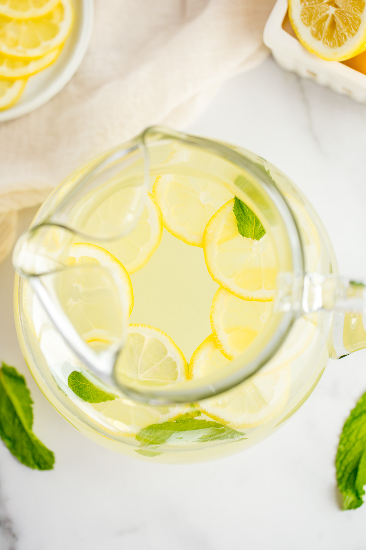 A large glass pitcher filled with homemade lemonade, lemon slices, and fresh mint leaves.