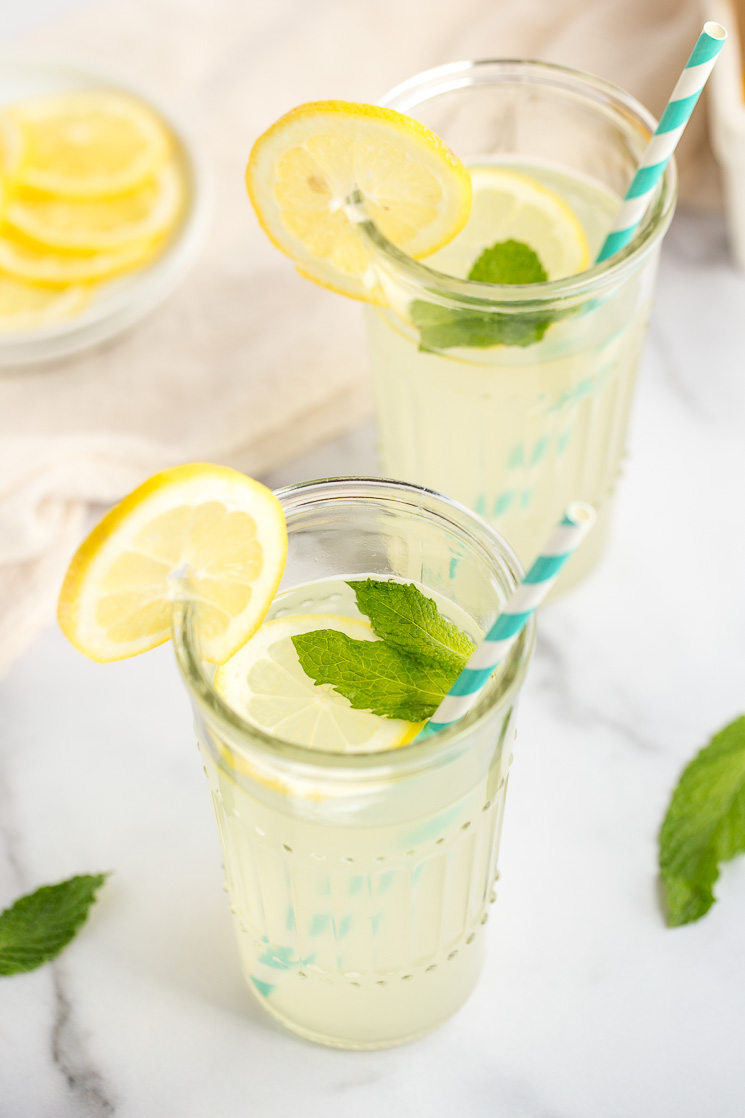 Two glasses of homemade lemonade with lemon slices, mint leaves, and straws.