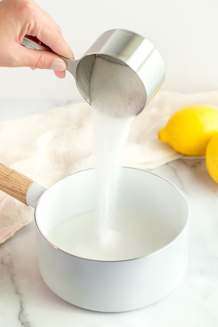 A hand adding a cup of sugar to a saucepan filled with water.