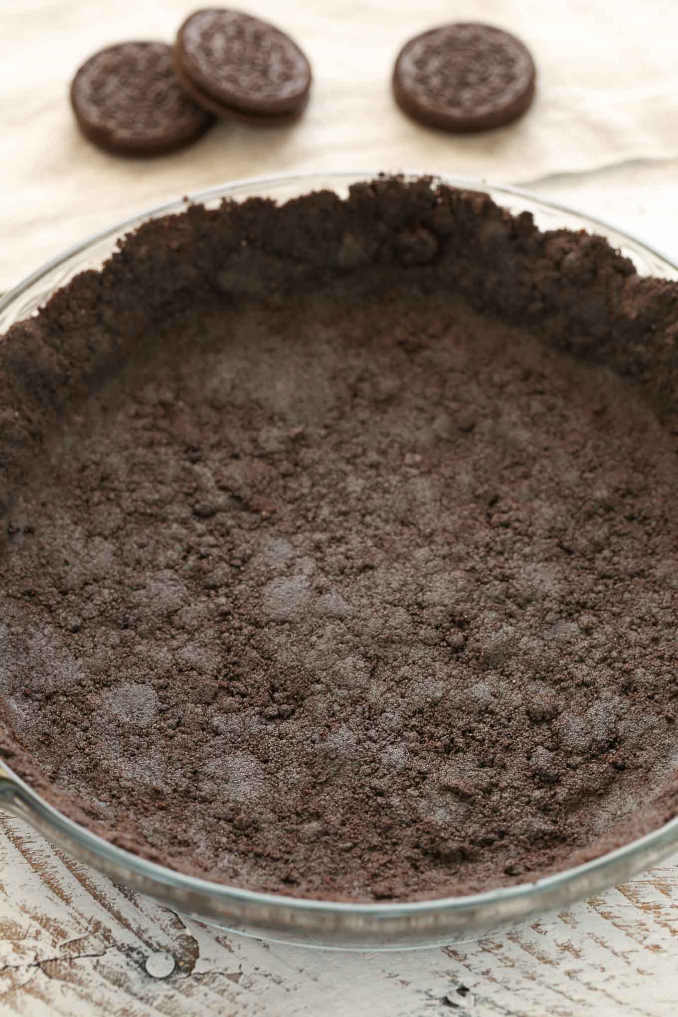 An Oreo pie crust in a glass pie plate. Three Oreos rest in the background. 