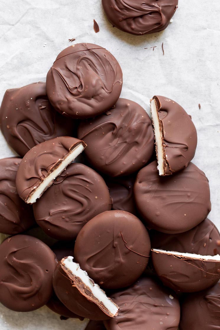 A pile of finished peppermint patties on a piece of parchment paper with some cut in half to show the inside detail.