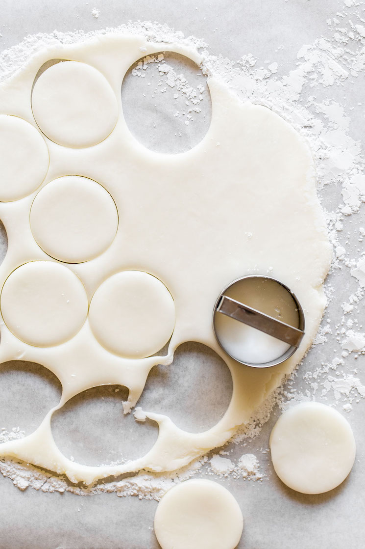 A piece of parchment paper with peppermint patty dough rolled out into a thin layer and circles being cut out of it.