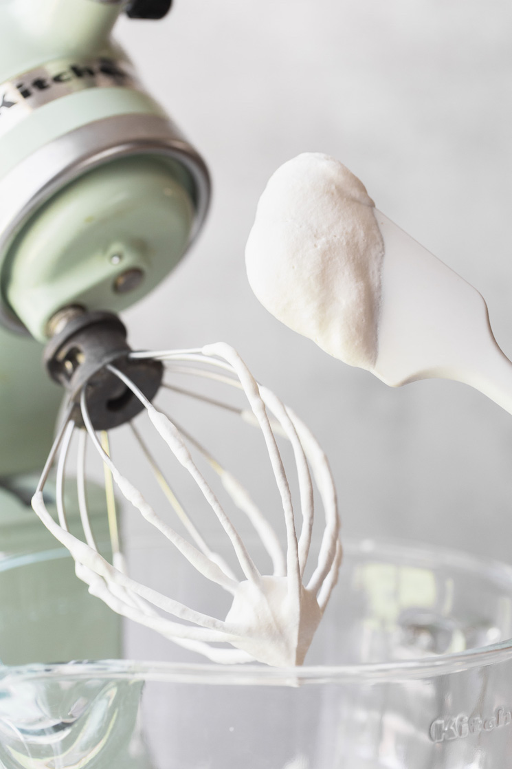 A stand mixer with a whisk and a rubber spatula covered in whipped cream.