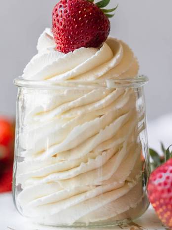 A small glass jar filled with whipped cream and topped with a strawberry.