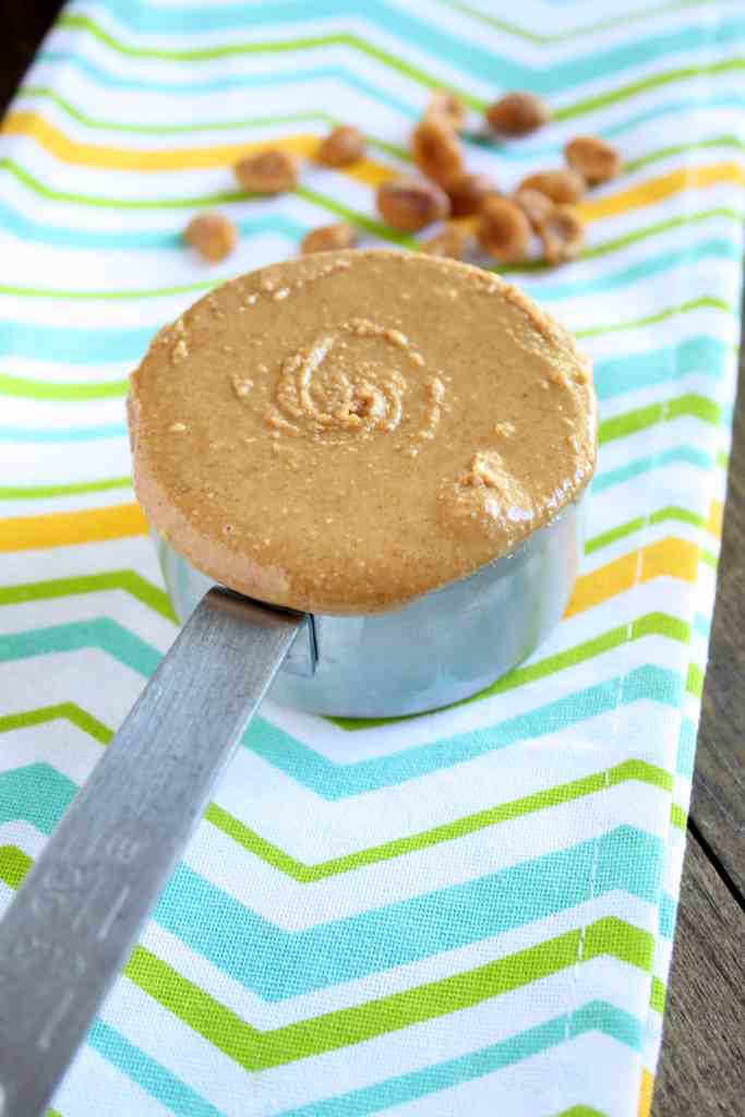 A measuring cup of honey peanut butter on a striped towel. 